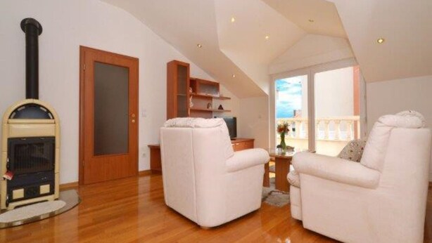 A spacious living room with a fireplace, two white armchairs, a wooden floor, and a view through a large window. - Bright Kaštela Apartment With Balcony and Private Parking (Kastela)