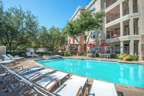 A pool area with lounge chairs and a building with balconies.