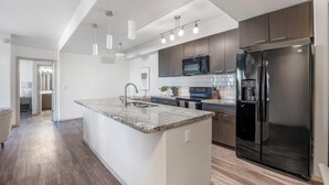 A modern kitchen with a central island, stainless steel appliances, and pendant lighting. - Landing | Stylish 2BD, Gym (Glendale)