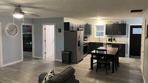 A modern kitchen with dark cabinets, a refrigerator, and a dining area with a table and chairs.