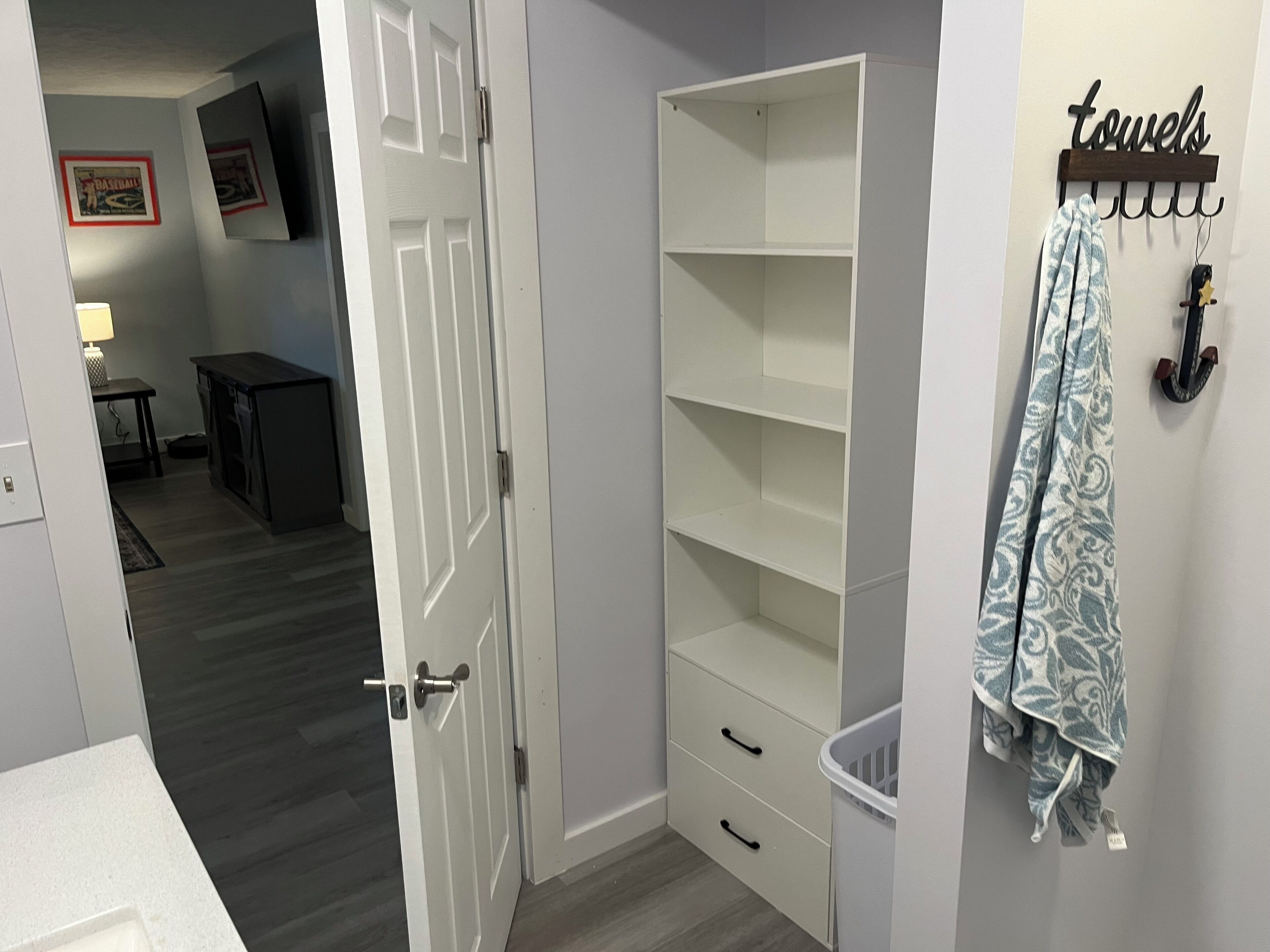 A room with a white door, a built-in shelving unit, a laundry basket, and a towel rack with a towel hanging on it.