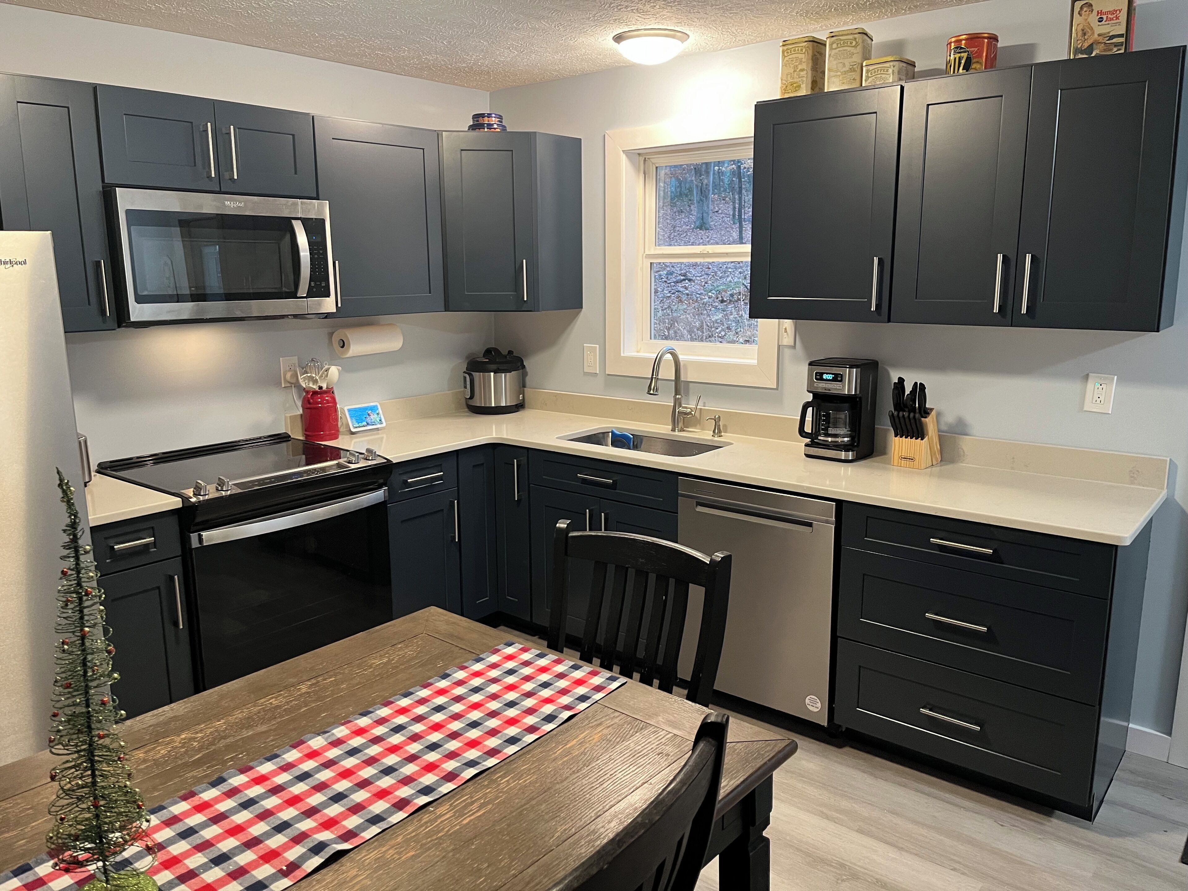 A modern kitchen with dark cabinets, a stainless steel microwave, a coffee maker, and a small window.
