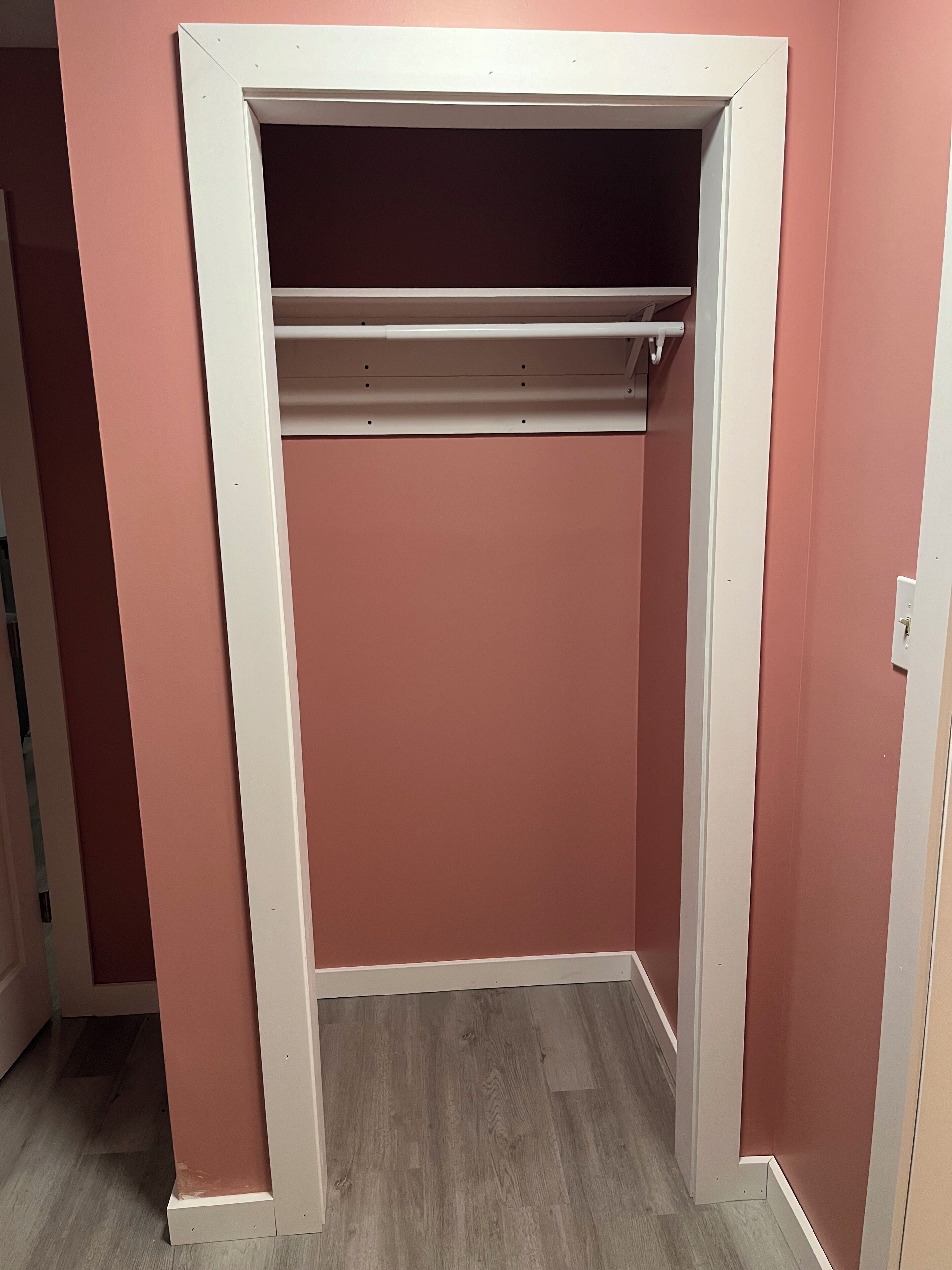 Ein Zimmer mit einer rosafarbenen Wand, einem weißen Türrahmen und einem Holzboden.