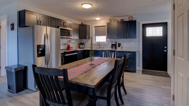A modern kitchen with dark cabinets, stainless steel appliances, and a wooden dining table.