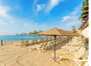 Hotel aan het strand met rijen ligbedden en parasols, een helderblauwe lucht en uitzicht op de zee en verre eilanden.