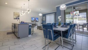A modern kitchen with a central island, dining area with blue chairs, and a large window with a view.