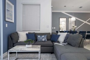 A modern living room with a sectional sofa, a coffee table, and a dining area with chairs and a table.