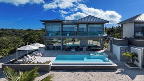 A modern two-story house with a swimming pool, outdoor seating, and a view of the surrounding landscape.
