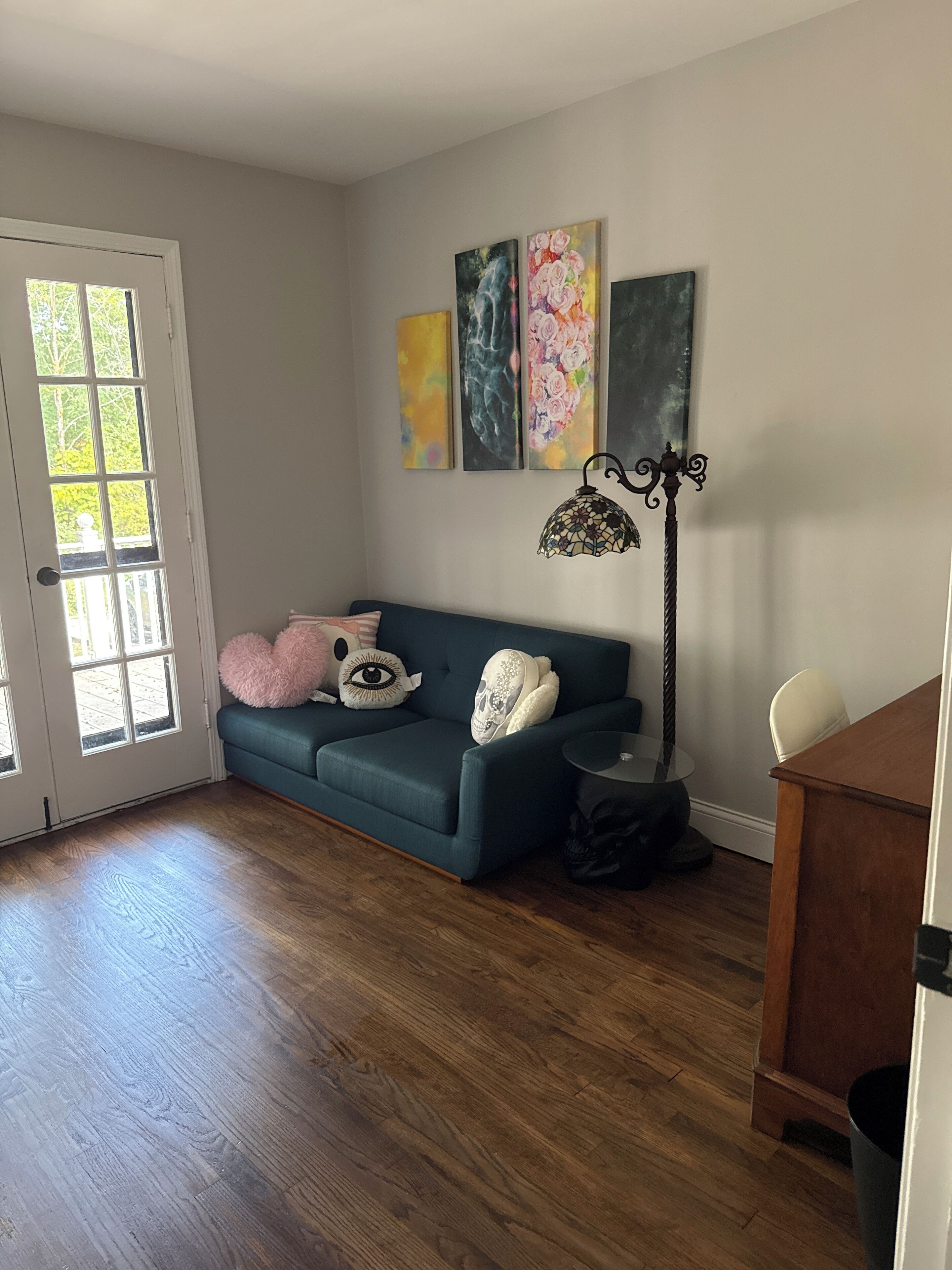 A room with a teal sofa, a black floor lamp, and three paintings on the wall.