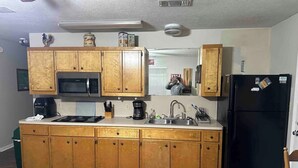 A compact kitchen with wooden cabinets, a black refrigerator, a microwave, and a coffee maker.