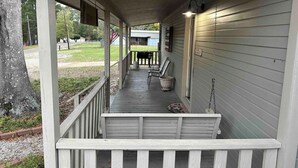 A covered porch with a railing, a bench, and a potted plant.