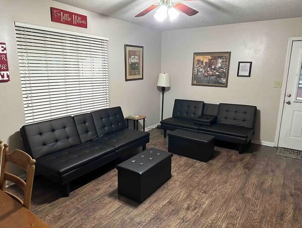 Ein Wohnzimmer mit zwei schwarzen Sofas, einem Couchtisch, einer Lampe und einem gerahmten Bild an der Wand.