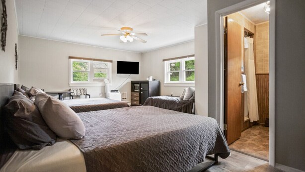 A bedroom with two beds, a ceiling fan, a TV, and a wooden door leading to a bathroom. - Double Queen + Twin | Motel Suite Near Wellsboro (Wellsboro)