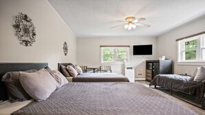 A bedroom with two beds, a ceiling fan, a TV, and a window with a view of greenery. - Double Queen + Twin | Motel Suite Near Wellsboro (Wellsboro)