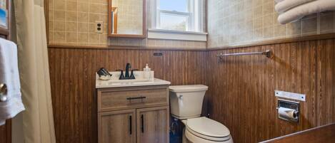 A bathroom with wooden paneling, a sink with a mirror, a toilet, and a towel rack.