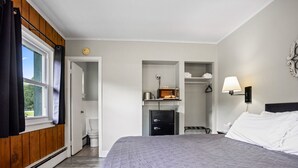Ein Schlafzimmer mit einem großen Bett, einem Kleiderschrank, einer kleinen Küchenzeile und einem Fenster mit Vorhängen.
