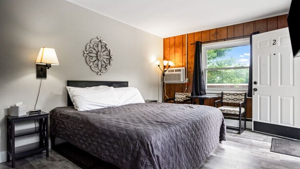 Ein Schlafzimmer mit Bett, Nachttischen, einer Wandlampe, einem Wandbild und einem Fenster mit Aussicht sowie einer Tür.