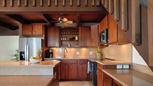 A kitchen with wooden cabinets, granite countertops, a stainless steel refrigerator, and a ceiling fan. - Modern condo oasis | Beach access | Stunning views (Kihei)