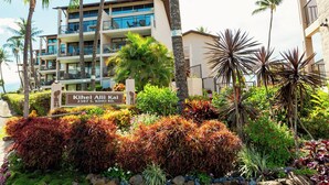 A hotel with a sign reading "Kihei Alii Kai 2387 S. KIHEI RD." It features a multi-story building with balconies, surrounded by tropical vegetation and palm trees. - Modern condo oasis | Beach access | Stunning views (Kihei)