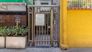 A metal gate with a sign, a tiled entrance, and a yellow wall with a white fence. - Studio 5min From Copacabana Beach Mvc901 (Rio de Janeiro)