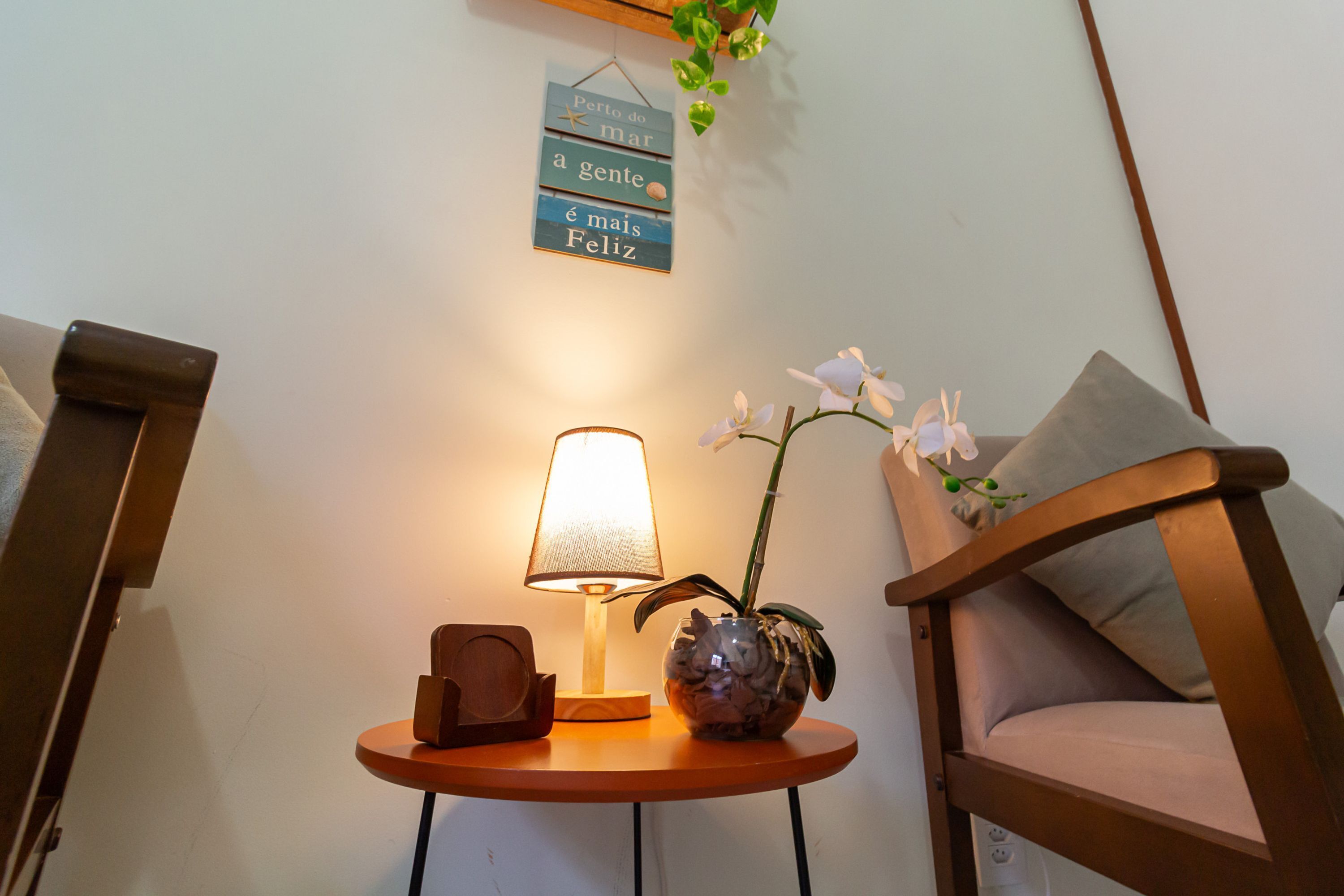 A cozy corner with a lamp, a wooden chair, a small table with a vase of flowers, and a wall sign.