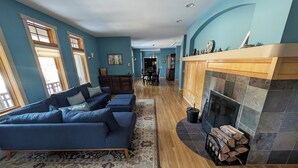 A spacious living room with a blue sofa set, a fireplace, and a dining area in the background. - Trout Lake Treehouse - A large, splendid, and private mountain home! (Trout Lake)