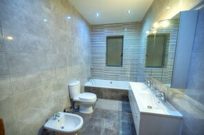 Ein modernes Badezimmer mit integriertem Bidet, Toilette, Badewanne und einem großen Spiegel.