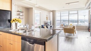 Eine moderne Küche mit einer großen Kochinsel, einer Essecke mit einer Couch und Blick auf die Stadt durch große Fenster.