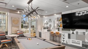 Ein modernes Wohnzimmer mit Billardtisch, gemütlicher Sitzecke, Fernseher und Küchenbereich.