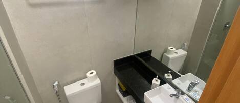 Ein Badezimmer mit Toilette, Waschbecken und Dusche. Über der Toilette befindet sich ein Fenster und über dem Waschbecken ein Spiegel.