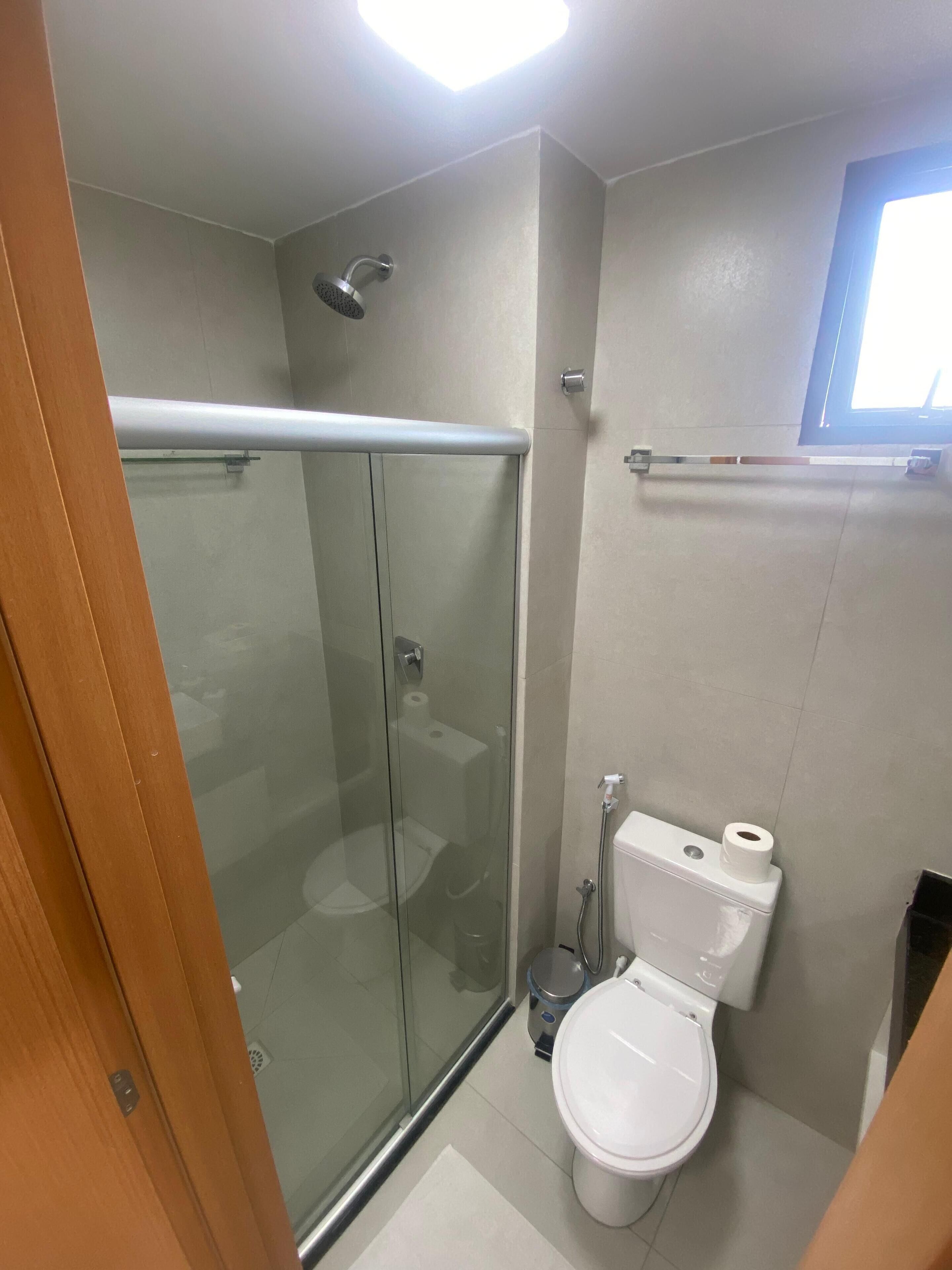 A bathroom with a glass-enclosed shower, a toilet, and a window.