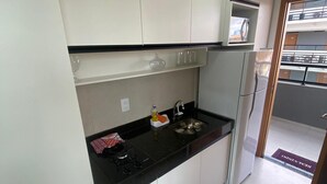 Una cocina moderna con armarios blancos, una encimera negra, un lavamanos de acero inoxidable y un refrigerador.