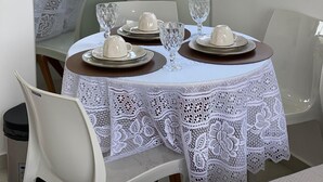 Un comedor con una mesa dispuesta para cuatro personas, con manteles de encaje blanco y platos marrones.