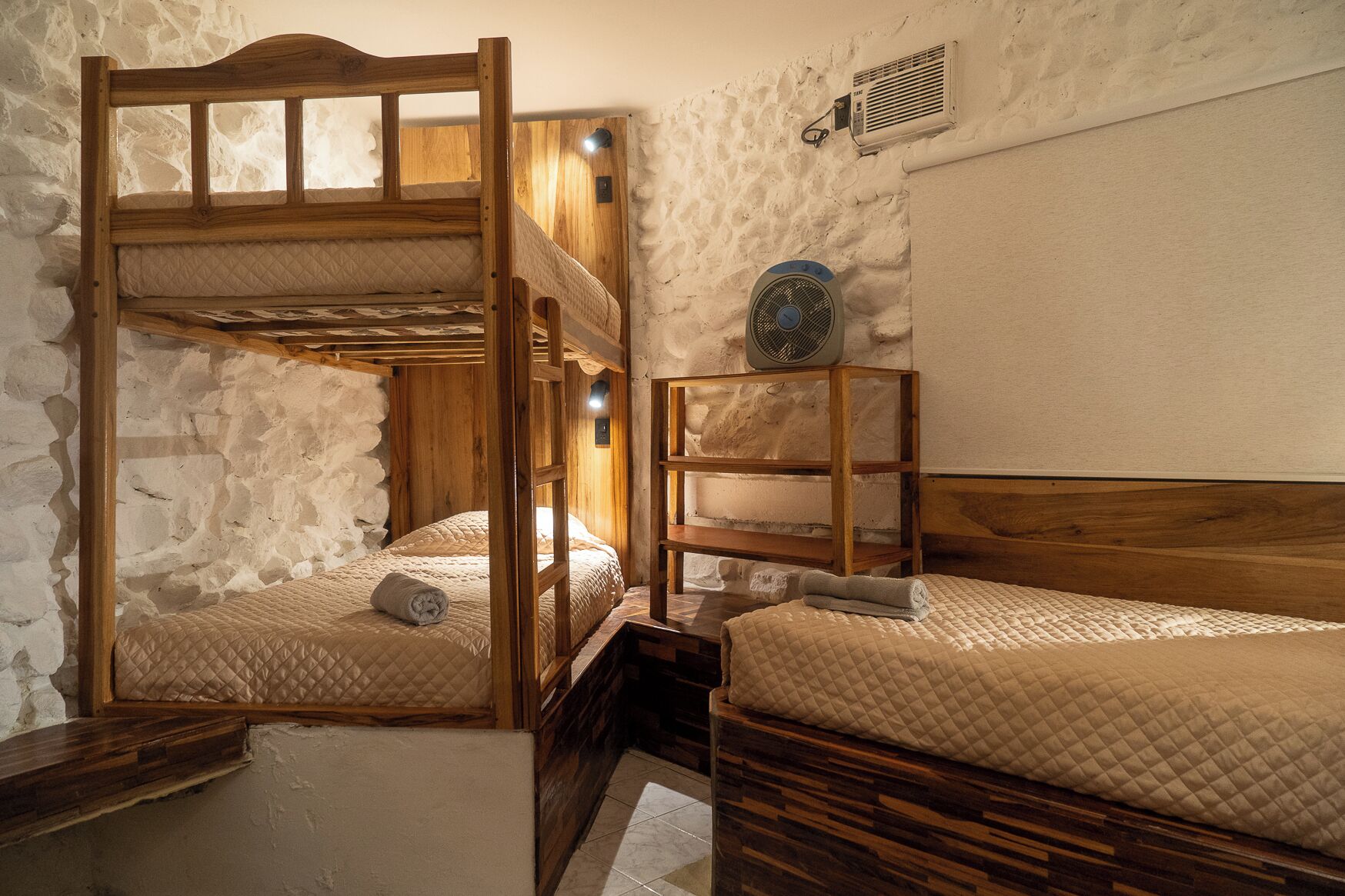 A rustic room with two bunk beds, a wooden shelf, and a wall-mounted heater.