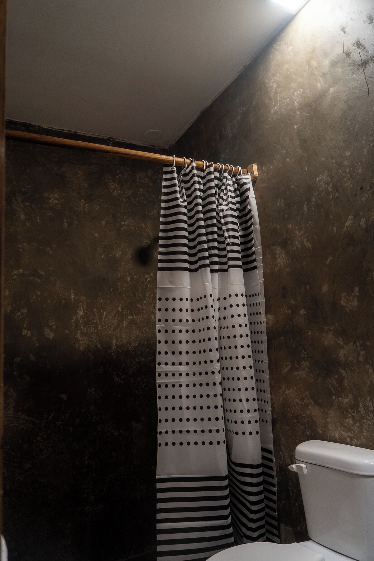 A bathroom with a striped shower curtain, a toilet, and a wooden towel rack.