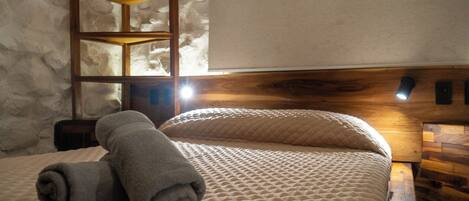 A neatly made bed with a rolled towel, a wooden headboard, and a wall-mounted shelf.