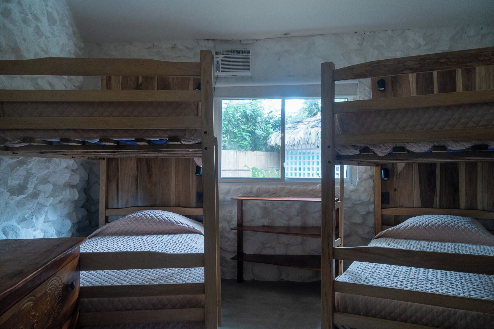 A bunk bed room with a stone wall, a window, and a wooden table.