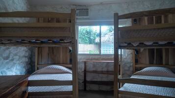 A bunk bed room with a stone wall, a window, and a wooden table.