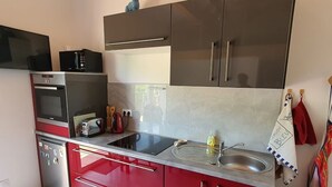 A modern kitchen with red cabinets, stainless steel appliances, and a large window. - L'Echappée du Camboux.  
Wellness discounts (Sainte-Cécile-d'Andorge)