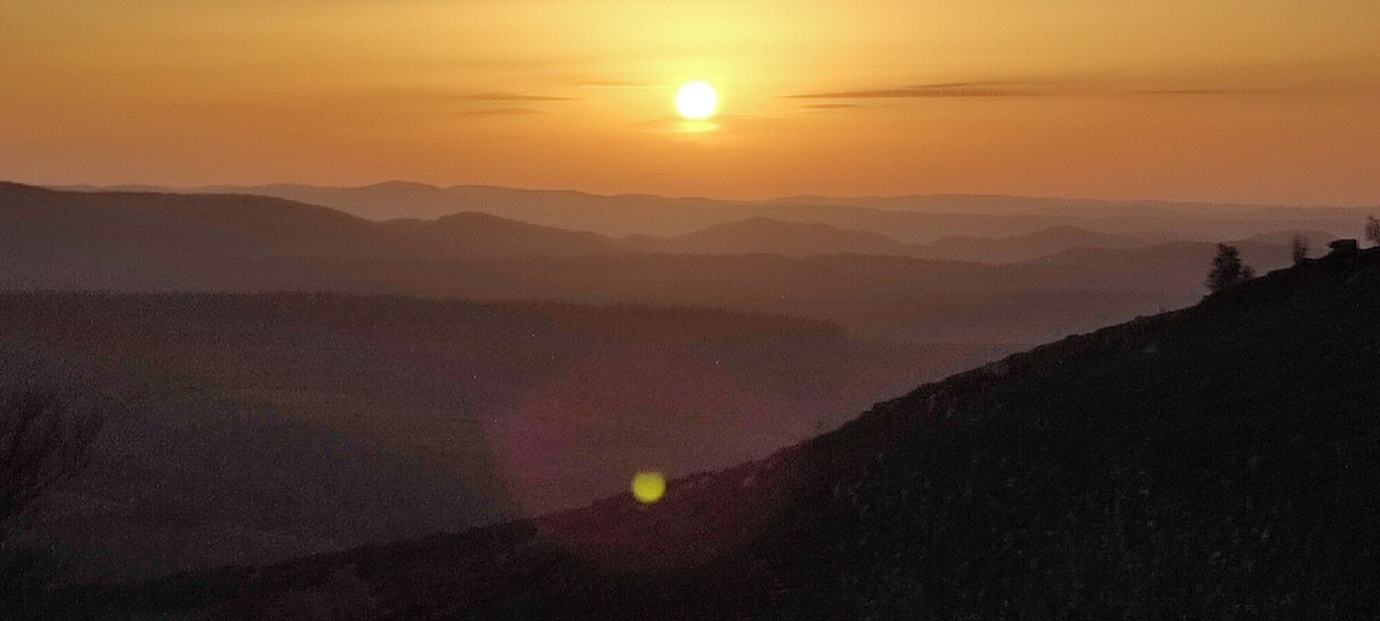 Paisaje montañoso al atardecer con el sol visible.