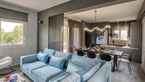 Ein modernes Wohnzimmer mit einem blauen Sofa, einem Essbereich mit Tisch und Stühlen sowie einer Küchenzeile mit Spüle und Arbeitsfläche.