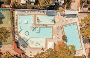 An aerial view of a swimming pool complex with multiple pools, sun loungers, and a tennis court. - The Charming Marina Village Tipo 3-3 Bedroom Villa 6 Persons (Comacchio)