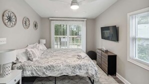 Une chambre à coucher avec un lit, un ventilateur de plafond, une télévision et une fenêtre avec des stores.