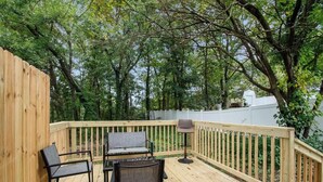 Une terrasse en bois, agrémentée de mobilier d’extérieur, entourée d’arbres et d’une clôture blanche.