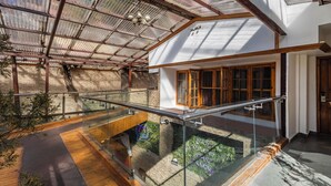 Un interior moderno con barandilla de vidrio, suelo de madera y vista a un jardín a través de un muro de cristal.