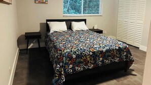 Une chambre à coucher comprenant un lit, une table de chevet, une fenêtre avec des stores, un tableau et une armoire.
