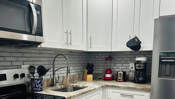 Une cuisine moderne avec des meubles blancs, un réfrigérateur en acier inoxydable, un four à micro-ondes, une cuisinière et une machine à café.