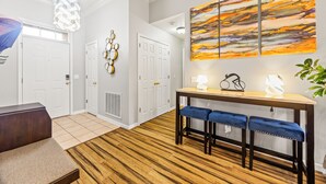 Et moderne interiør med trægulv, en bænk, et bord med klapstole, et abstrakt billede på væggen og en lampe i loftet.