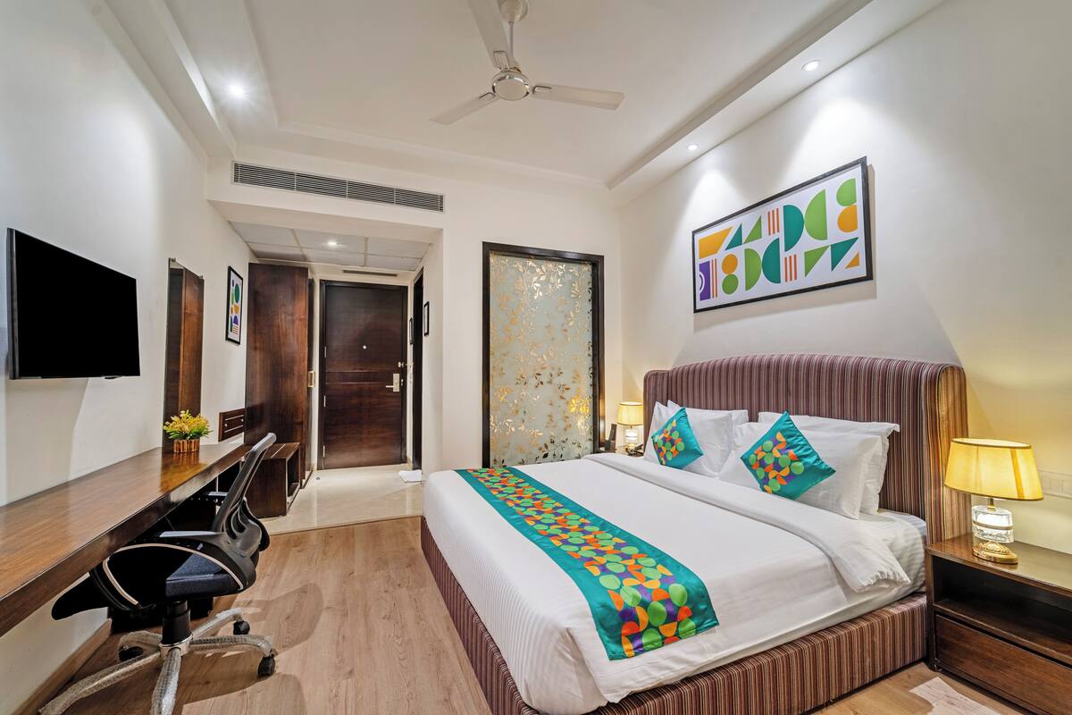 A hotel room with a large bed, a desk with a chair, a television, and a ceiling fan.