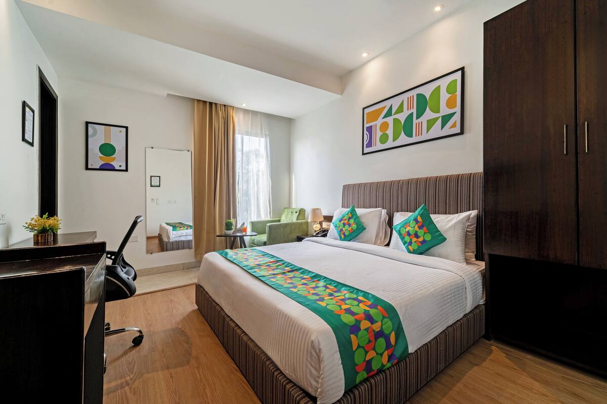 A hotel room with a large bed, a desk, a chair, a wardrobe, and artwork on the walls.